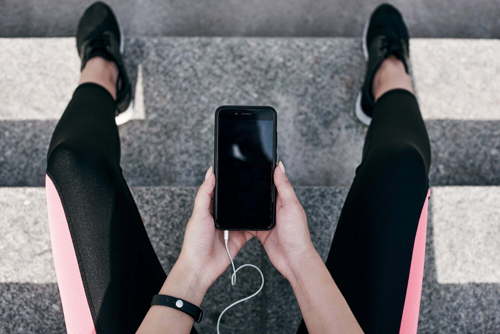 Fitness runner on mobile smart phone app tracking progress listening to music with earphones for