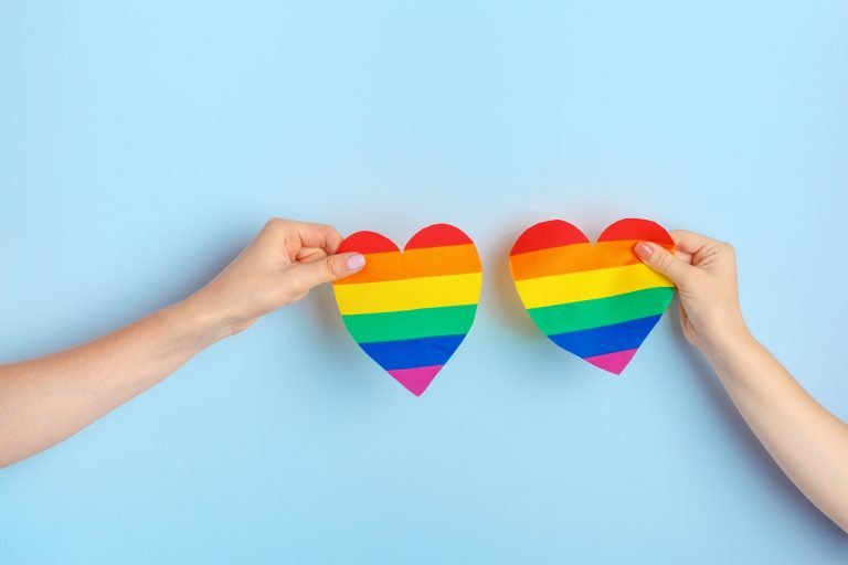 Gay love. Human hand holding a rainbow paper heart