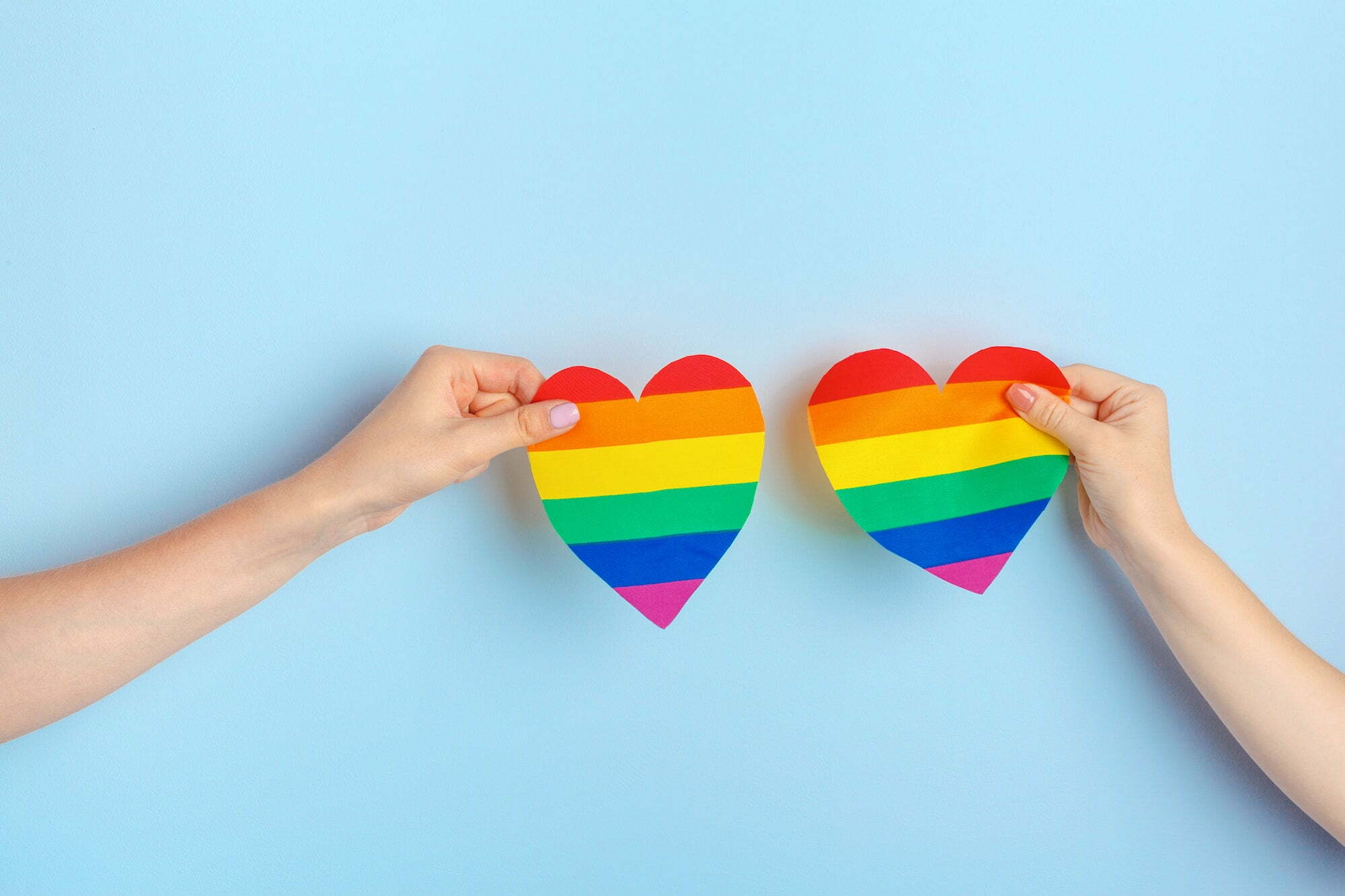 Gay love. Human hand holding a rainbow paper heart
