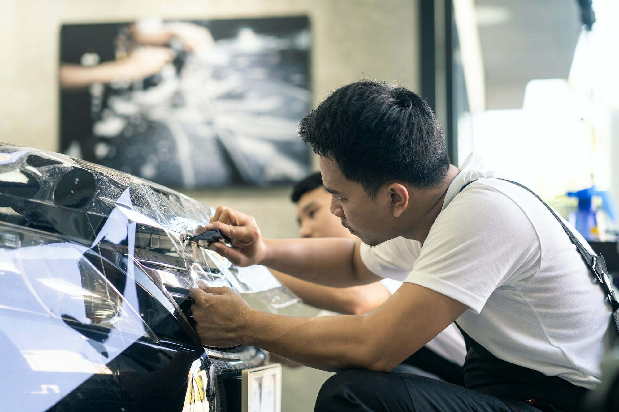 Two Asian car film protection male worker installing film to black color car in garage